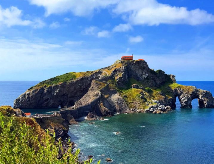 San Juan de Gaztelugatxe in full sun with the sea arch cut through the cliff on the right